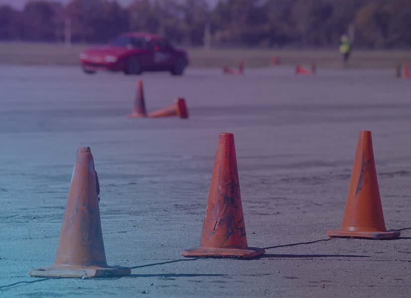 Image showing orange cones laid out on a closed-circuit autocross course with a competitor's car in the background running the course.