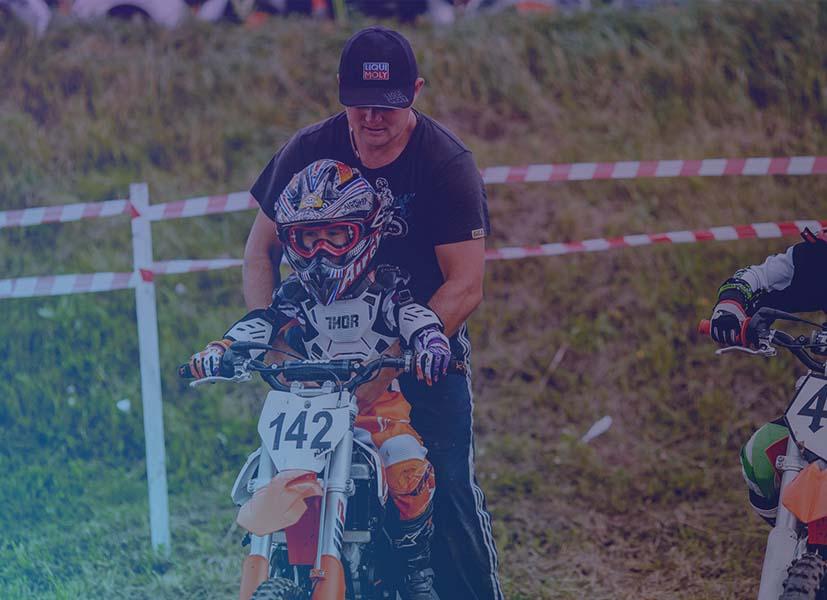 Image of a kid on a dirt bike being led by a camp instructor at dirt bike camp event.