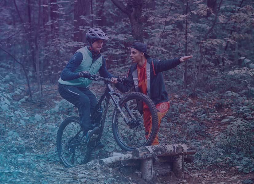 Image of a bike camp participant being coached by a camp monitor through a mountain bike obstacle.