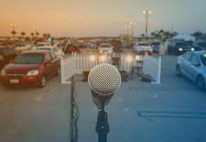 Image of a microphone on a stage setup in front of a crowd in cars attending a drive in event.