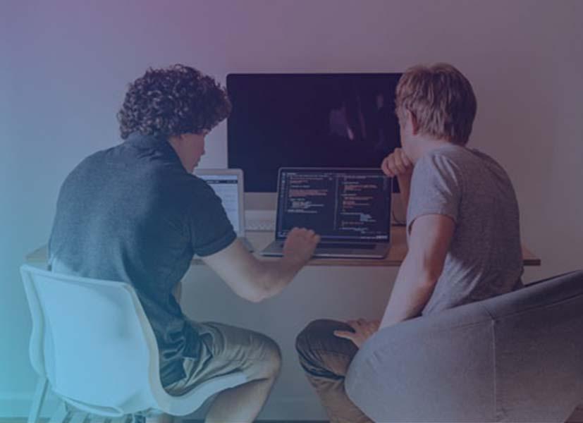 Image of 2 young man concentrated in front of laptops and computer monitors who are participating in a Hackathon event.