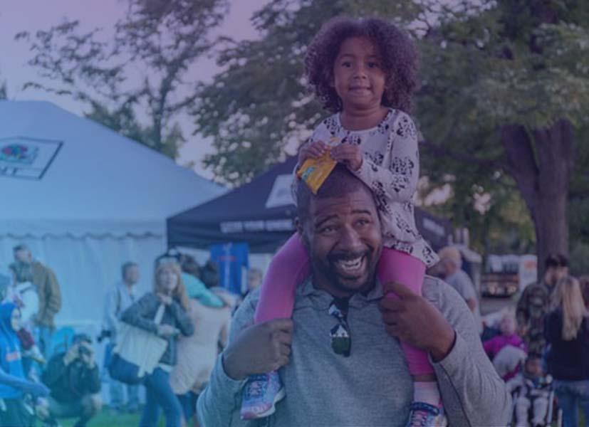 Image of a young girl on her father's shoulders attending a street festival event.