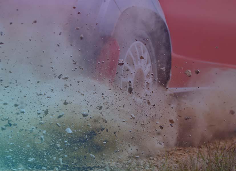 Image of a rally car's rear wheel raising up dirt and stones during the start of a rally event stage.