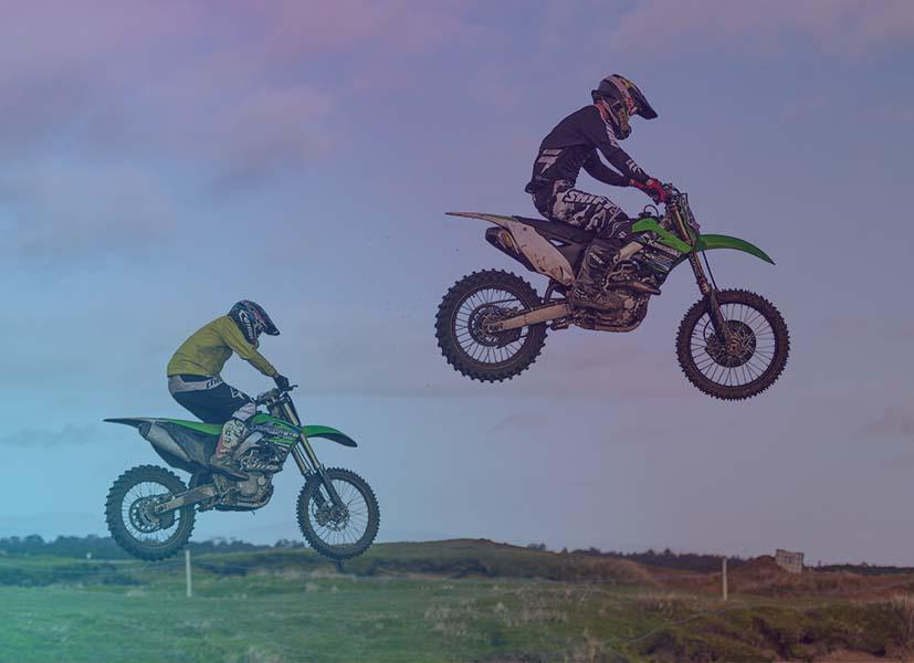 Image of 2 motorcross rider jumping over an obstacle during a motorcross racing event.