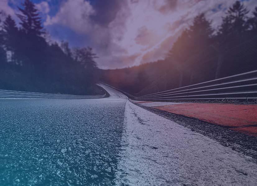 Image of a race track viewed from the pavement looking out on a long straightaway.
